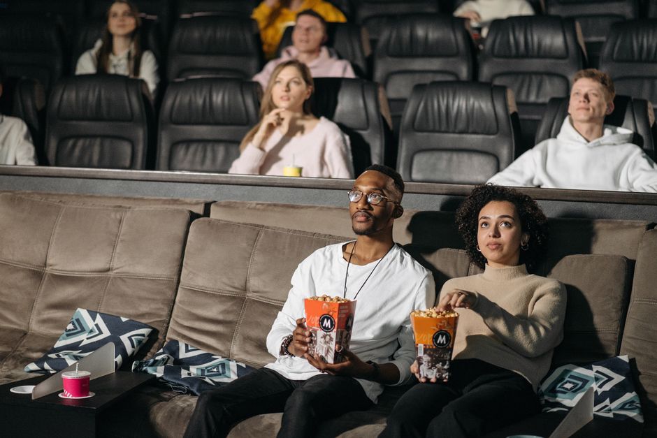 A couple enjoys popcorn while watching a movie in a cozy cinema environment, surrounded by others.