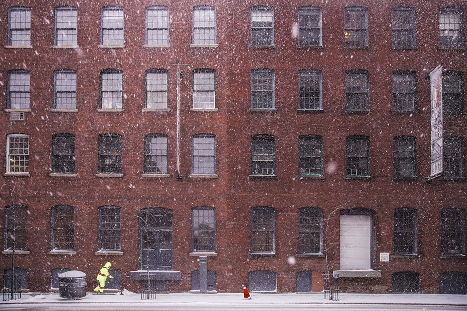 A person walks past a brick building during a snowstorm in an urban setting.
