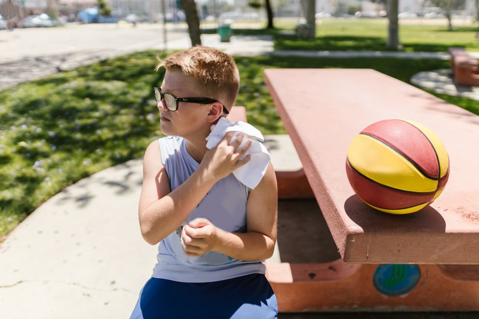 A young boy sits at a park bench with a basketball, enjoying a sunny outdoor break.