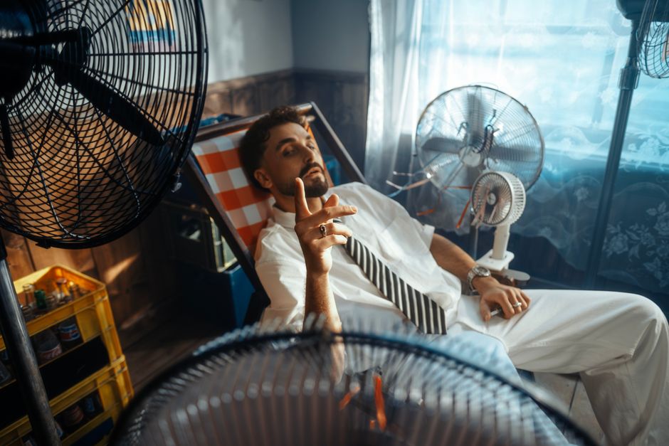A man in a white suit lounges in a warm room, cooled by multiple fans.