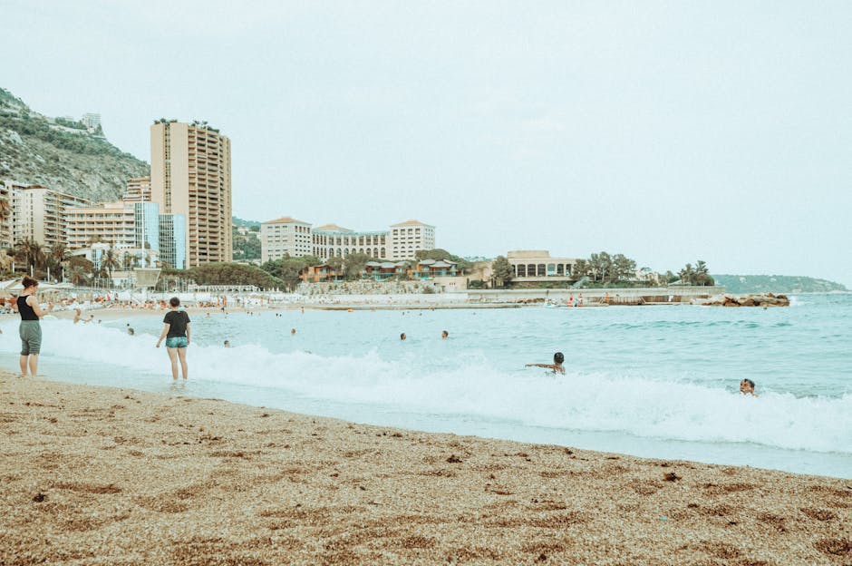 A lively beach scene with tourists enjoying the Mediterranean coast, featuring waves and urban skyline.
