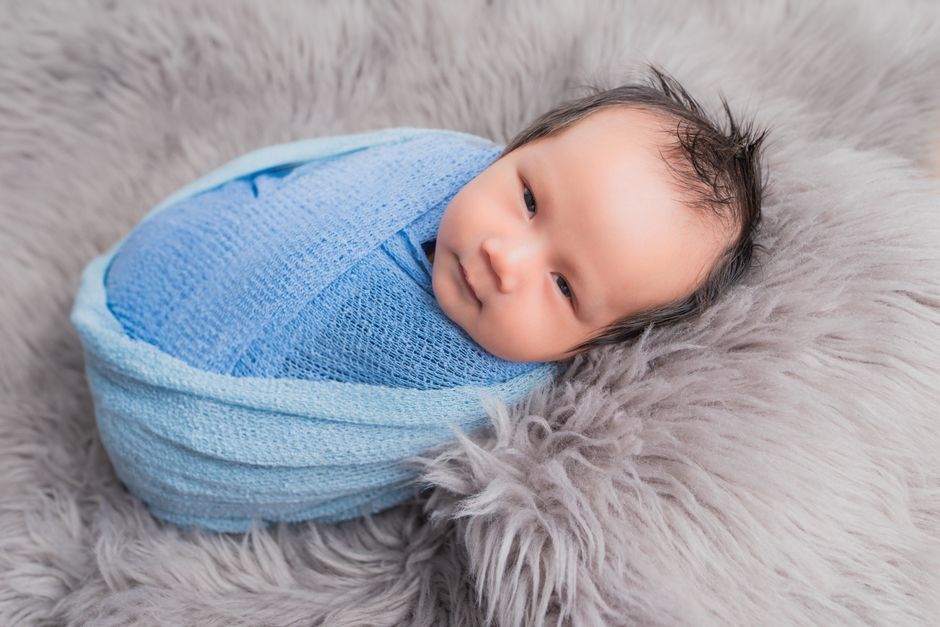 Adorable newborn wrapped in a blue blanket lying on a plush fur blanket for a cozy portrait.