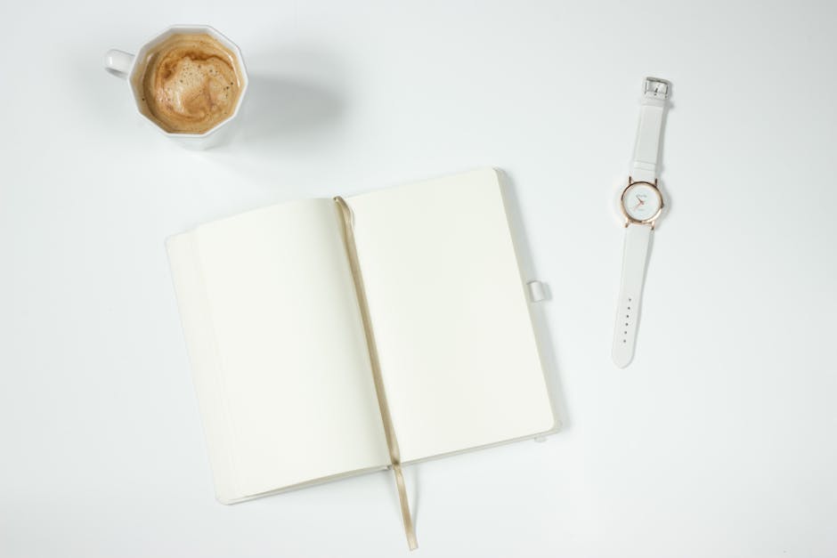 Top view of a minimalist workspace with coffee, open notebook, and wristwatch on a white background.