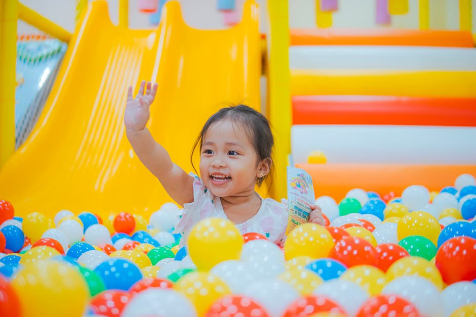 Happy child playing in a vibrant ball pit, surrounded by colorful balls and a slide, expressing fun and joy.