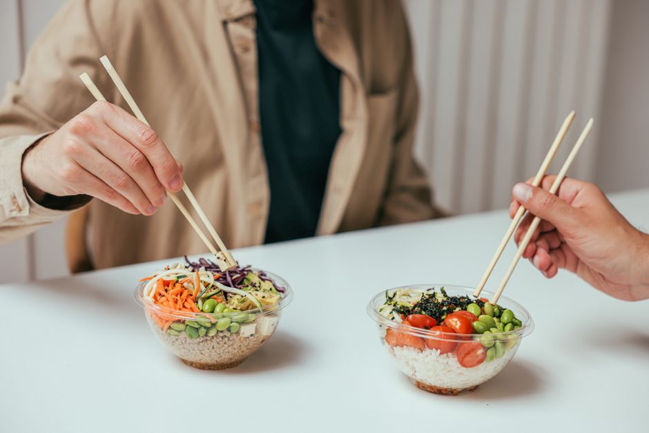 Close-up of two people enjoying healthy rice bowls with chopsticks, featuring fresh vegetables and rice.