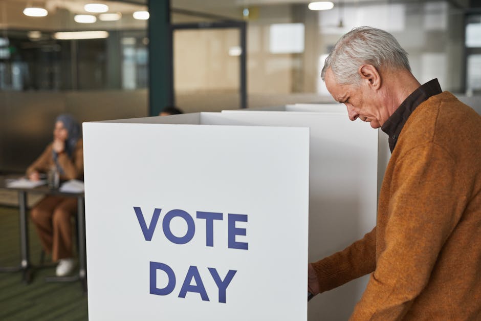 Senior man in brown sweater voting at an indoor polling station on election day.