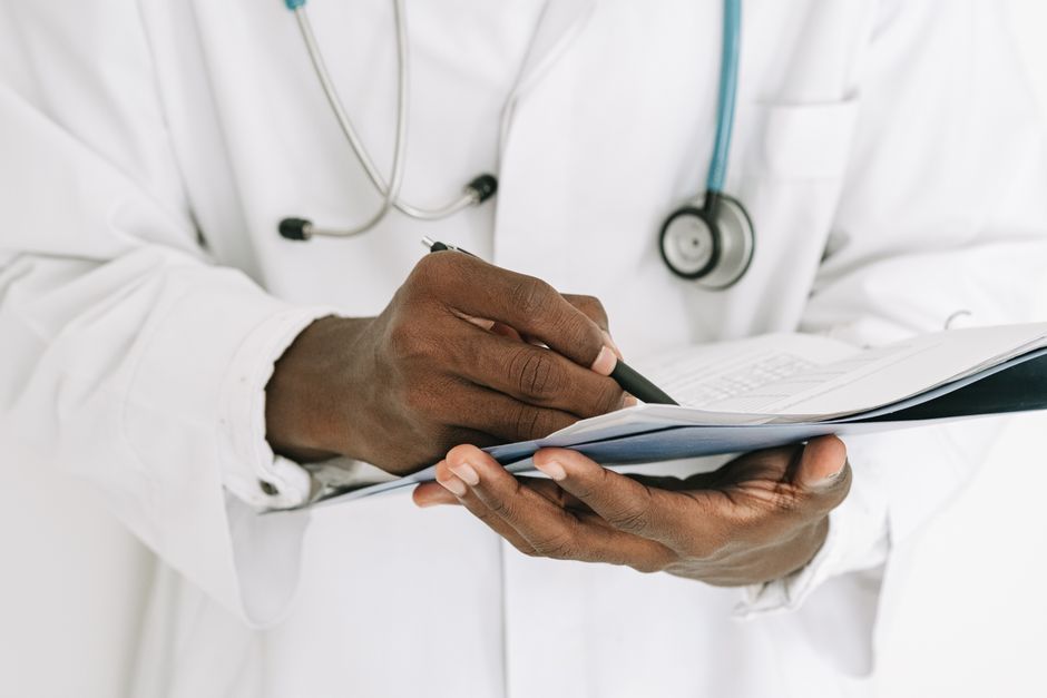 Professional doctor writing on a clipboard with a stethoscope in a medical office.