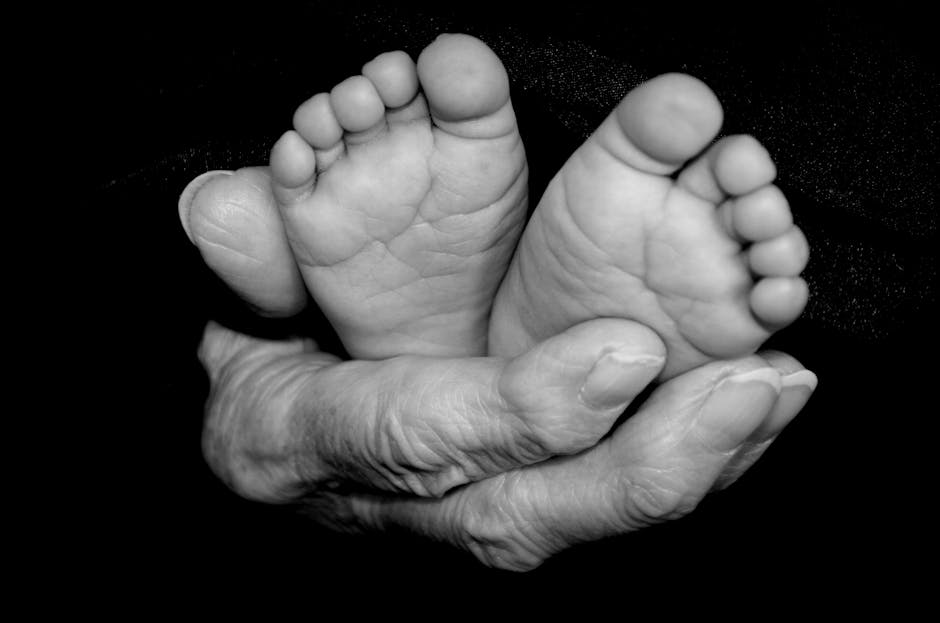 A touching black and white close-up of a baby's feet cradled in elderly hands, symbolizing care and connection.