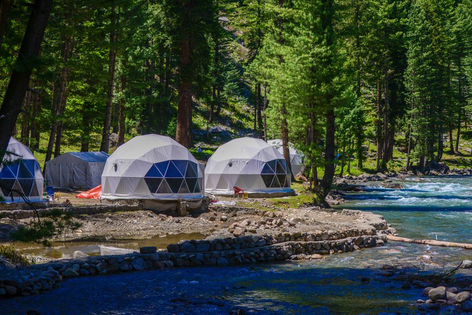 Geodesic tents along a river in Kumrat Valley's vibrant forest glamping site.