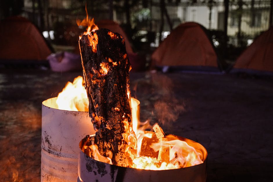 Glowing campfire in a barrel among tents, creating a warm nighttime ambiance.