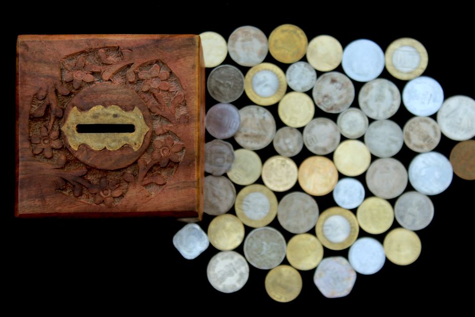 Top view of a vintage wooden piggy bank and assorted coins on a black surface, symbolizing savings and wealth.