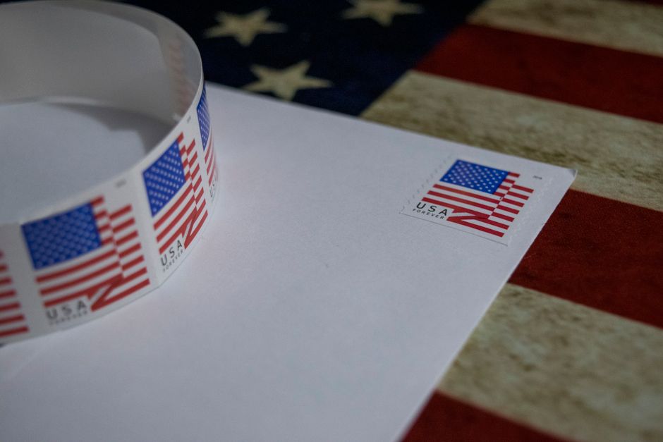 Close-up of USA flag postage stamp on white envelope with American flag background, symbolizing patriotism.