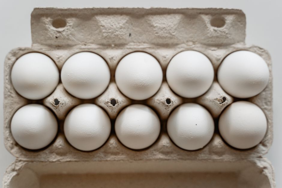 A dozen white eggs neatly arranged in a cardboard carton, viewed from above.