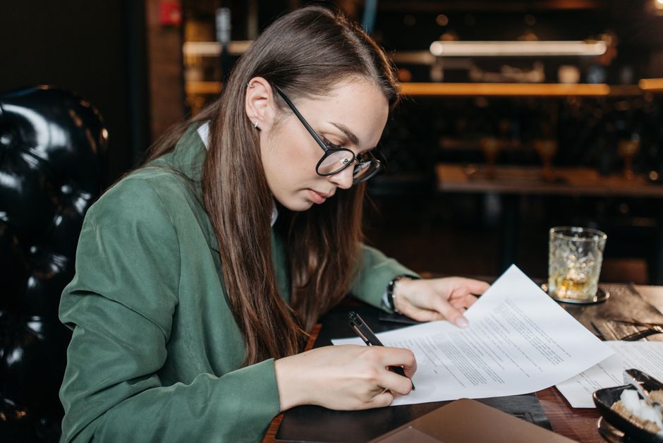 Focused businesswoman in green attire signing important documents at her desk.