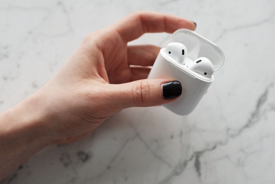 A close-up view of a hand holding white wireless earbuds in a case on a marble surface.