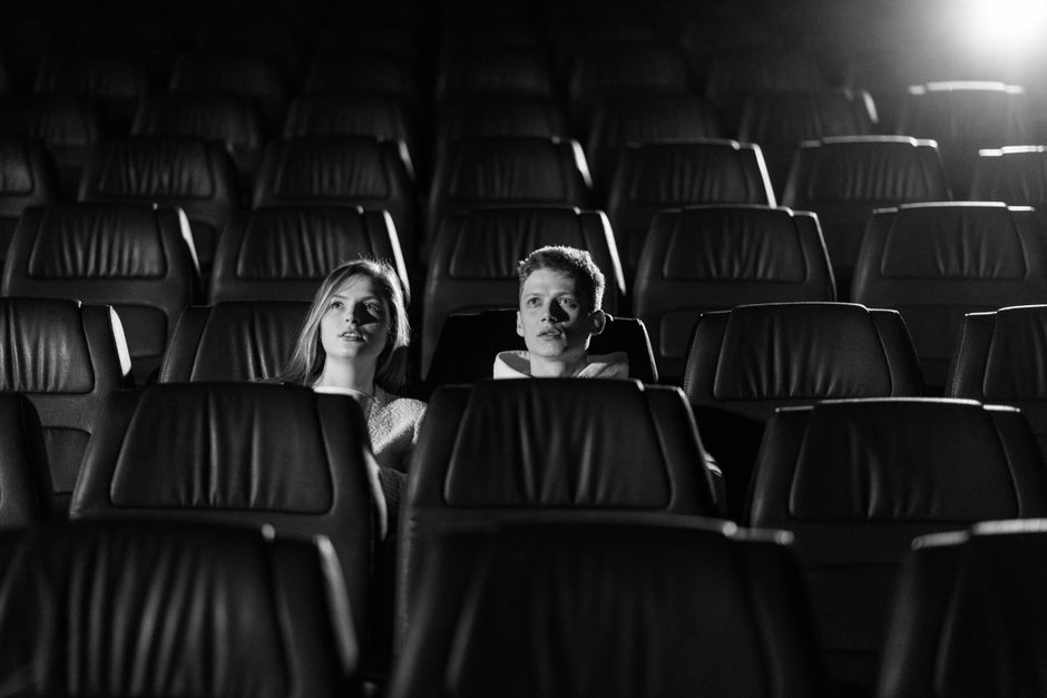 A couple watching a movie in an empty theater with monochrome lighting.