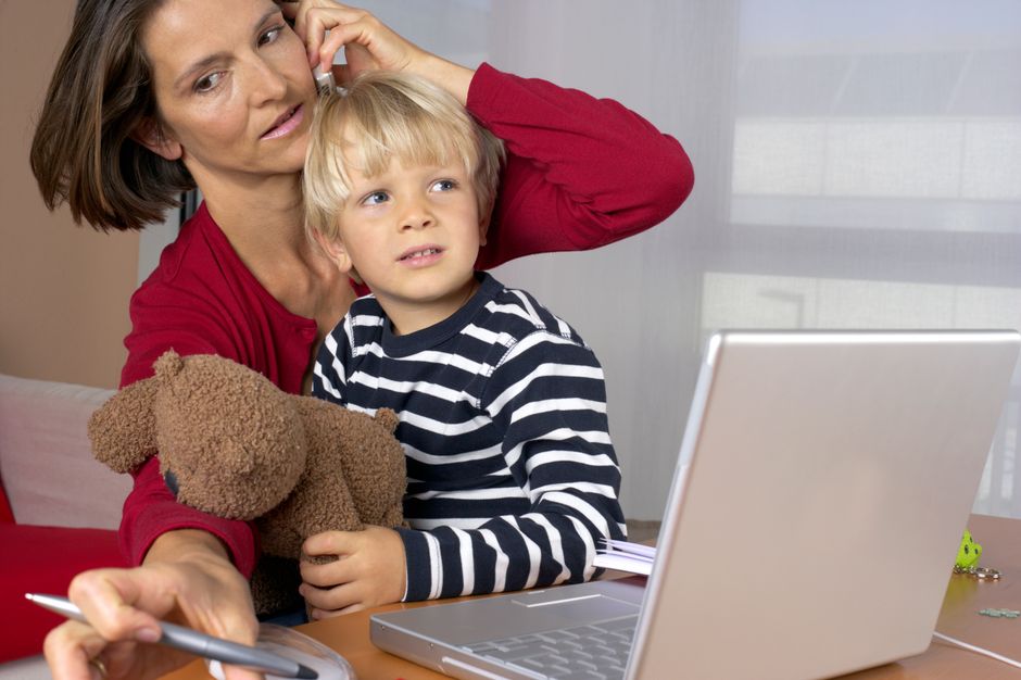 A mother multitasks by talking on the phone while managing work and child at home.