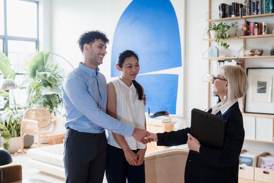 Smiling couple meeting with a real estate agent in a modern living room setting.