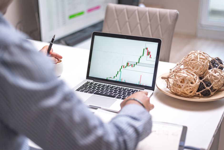 Person analyzing stock market trends on laptop in a modern home office setting.