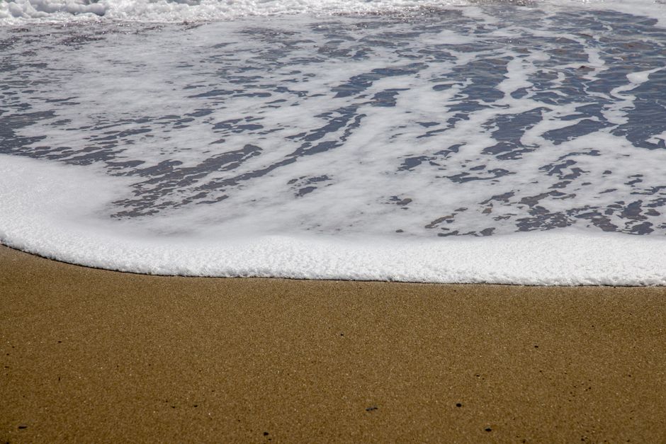 Gentle ocean waves creating foam as they meet the sandy beach on a sunny day.