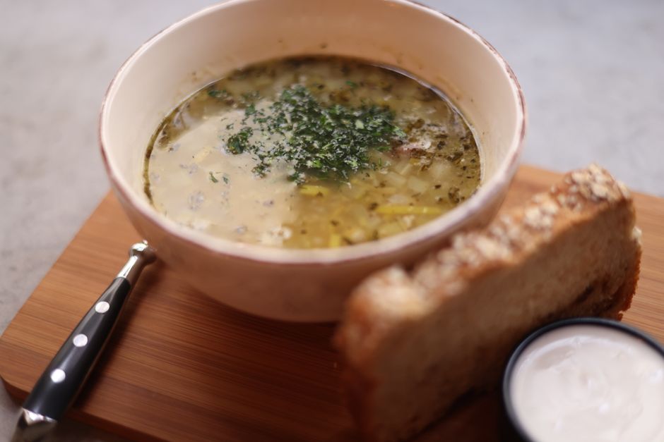 A bowl of delicious chicken soup served with fresh bread on a wooden board.