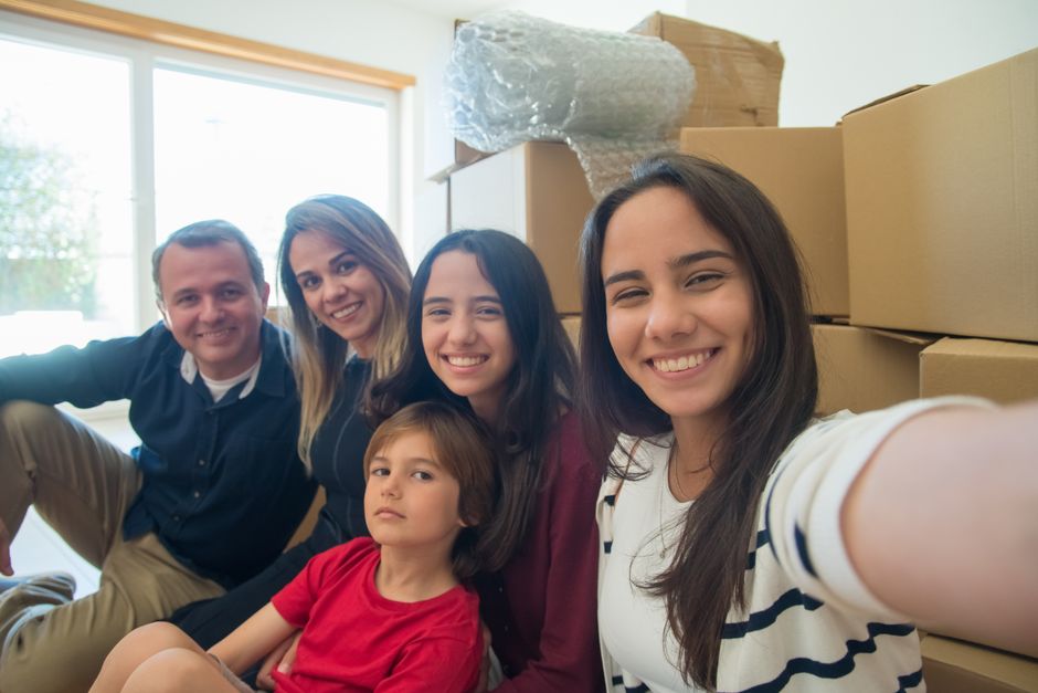 A joyful family takes a selfie together surrounded by moving boxes, capturing a memorable moment.