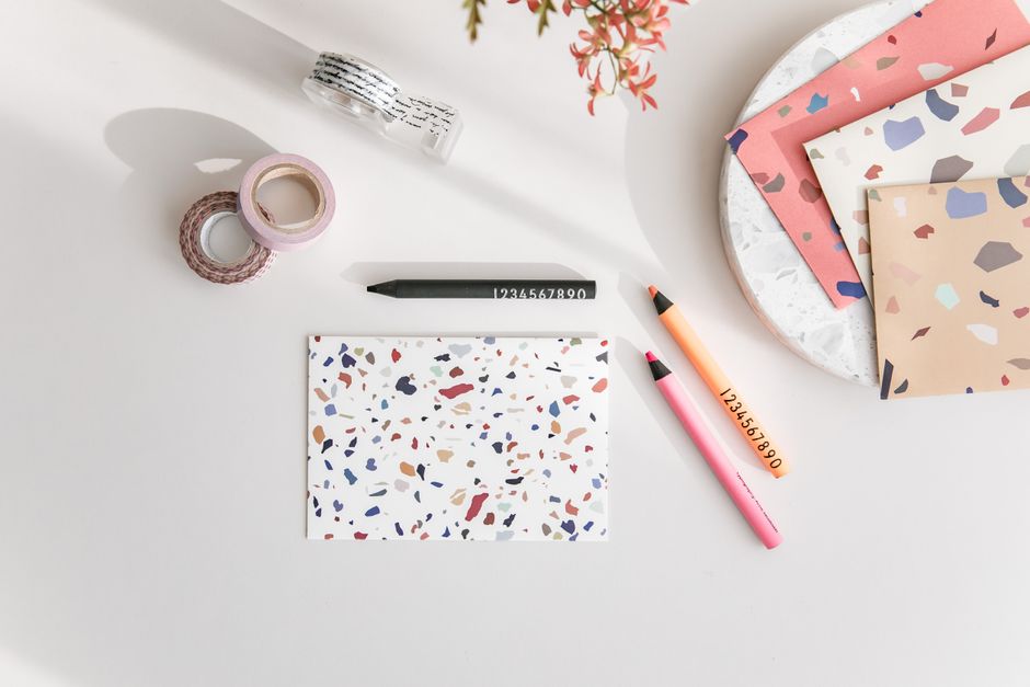 Aerial view of a terrazzo notebook, colorful pencils, and washi tape on a desk.