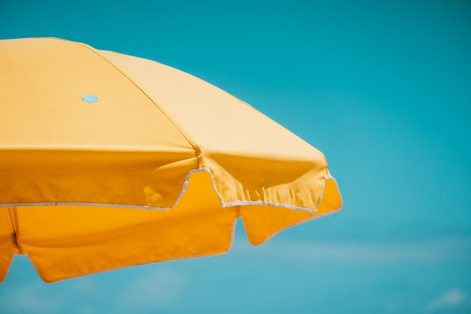 A vivid yellow beach umbrella set against a clear blue sky, capturing the essence of summer.