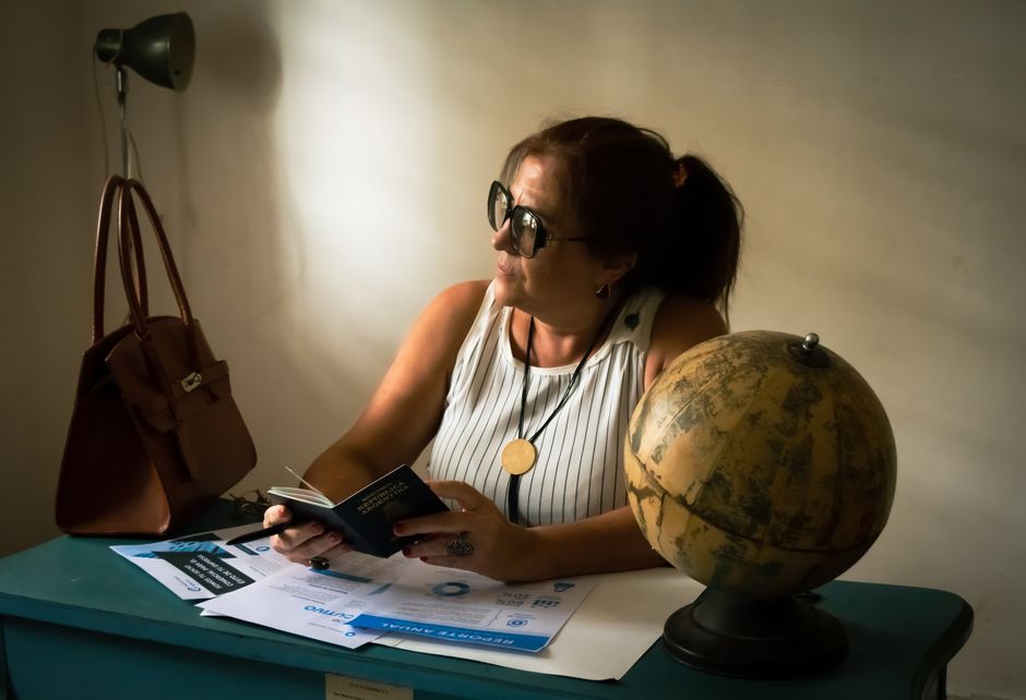 A woman seated indoors reviews travel documents beside a globe, suggesting travel planning.
