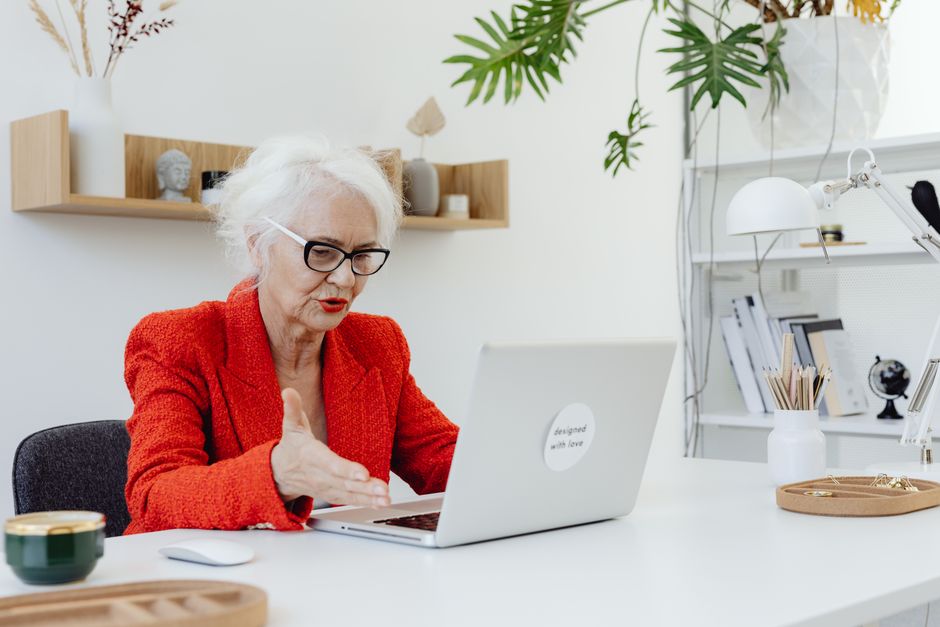 Confident senior businesswoman in a red blazer working on a laptop at her stylish office desk.