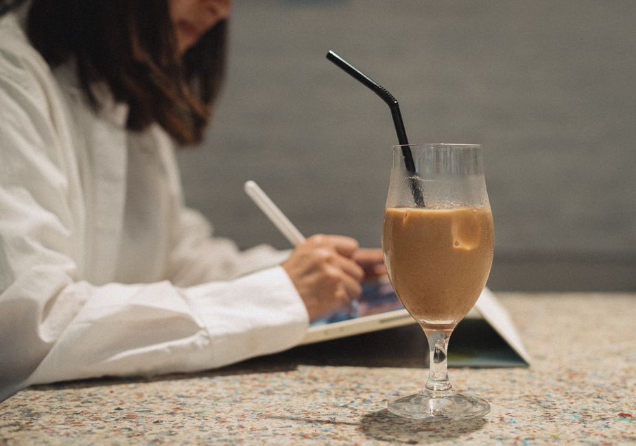 A woman writes in a notebook at a Tokyo café, next to a refreshing iced coffee.