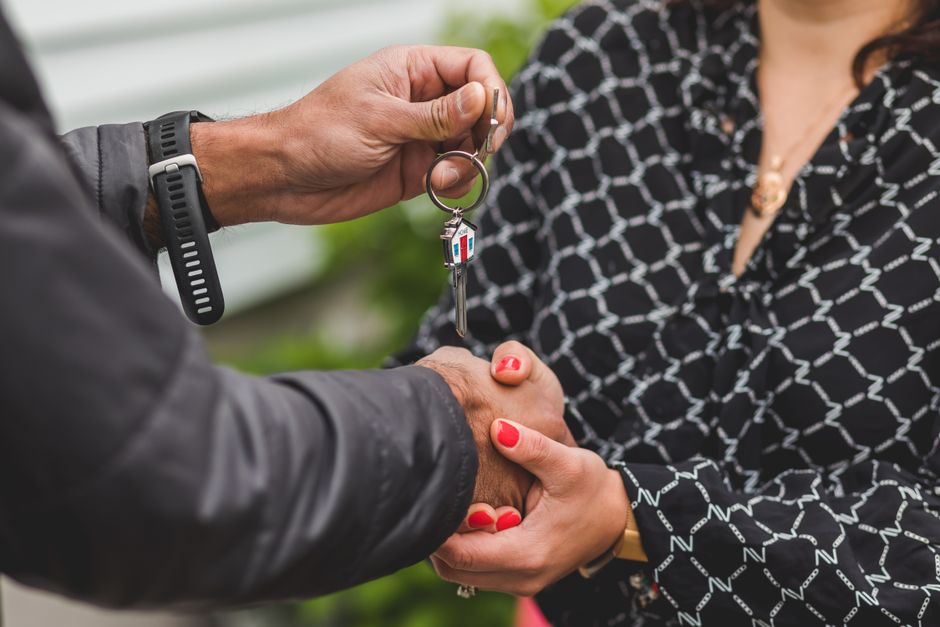 A close-up shot of hands exchanging a house key, symbolizing real estate transactions or new home ownership.