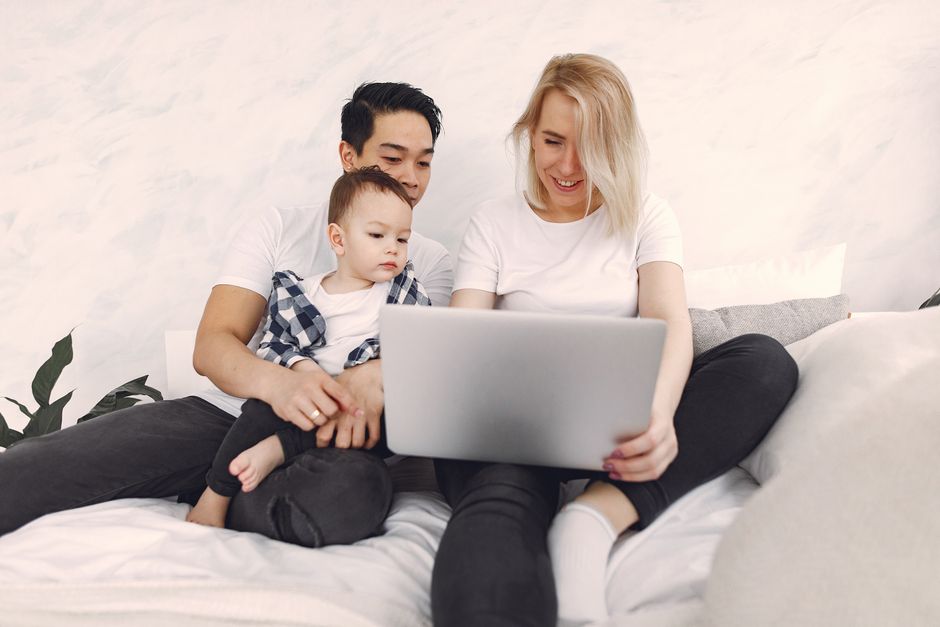 Family enjoying quality time using a laptop together on a bed at home.