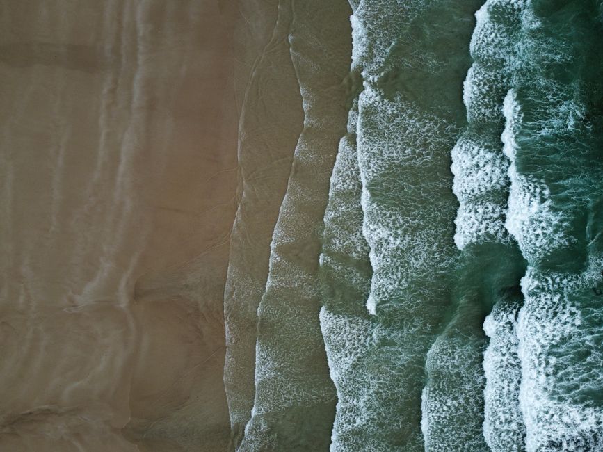 Aerial shot of ocean waves crashing on a sandy beach creating textured patterns.