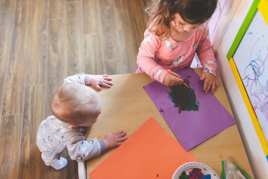 Two young children painting with vibrant colors at home. Captured from above.