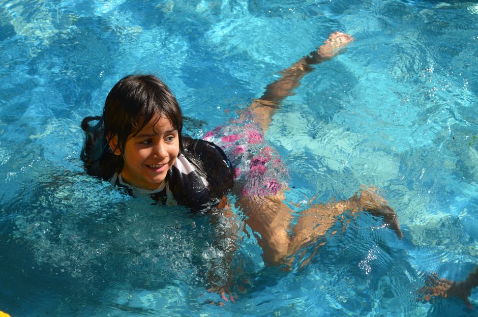 A cheerful child swimming and smiling in a sunlit pool, enjoying a summer day.