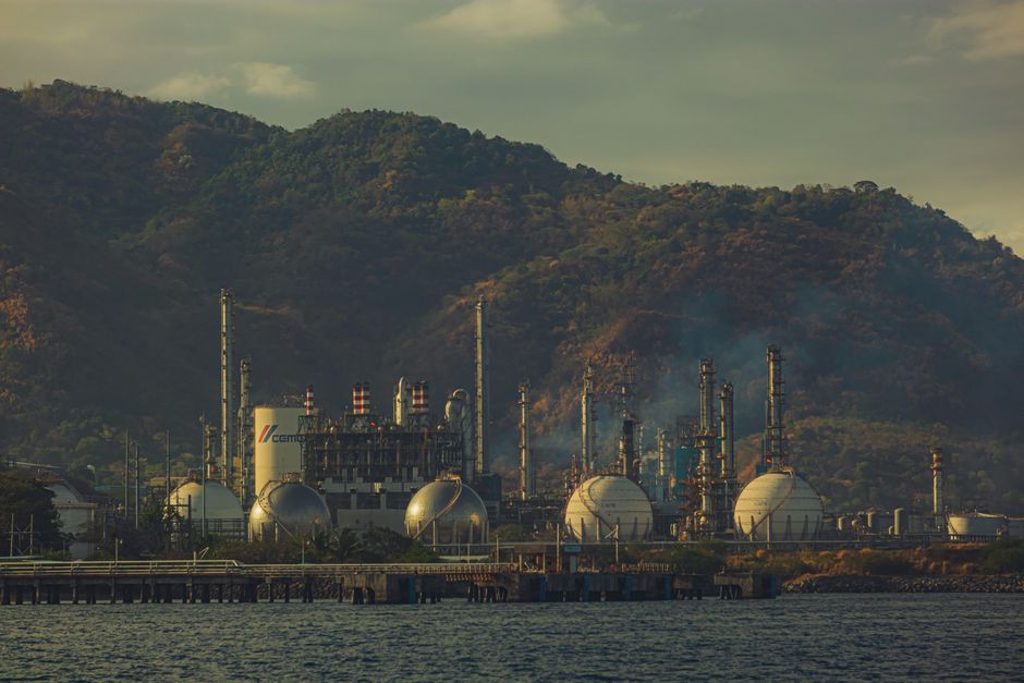 Industrial factory near mountains by a river, showcasing chimneys and infrastructure.