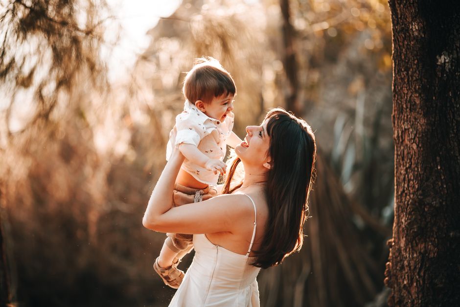 Heartwarming moment of a mother lifting her child in a sunlit park. Perfect for themes of love and family.