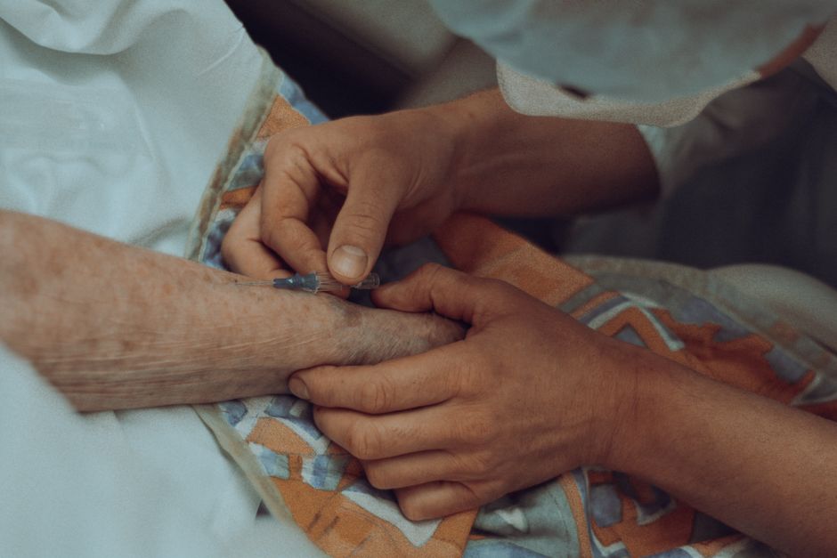 A healthcare professional administers an injection to an elderly patient in a hospital setting.
