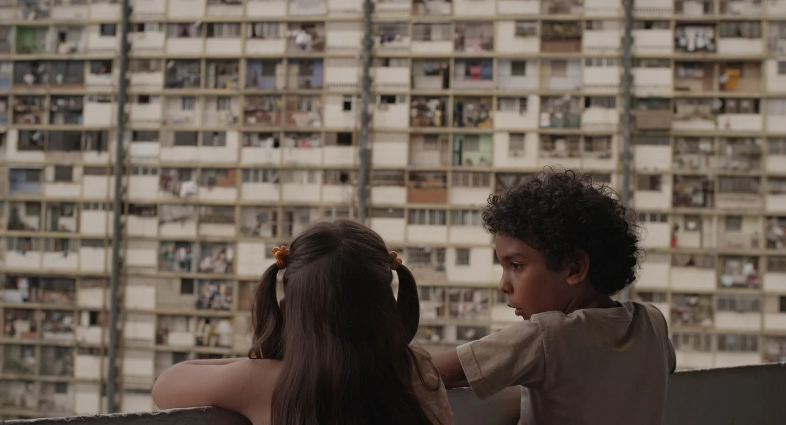 Junior y su amiga miran desde un balcón un enorme y denso bloque de edificios multifamiliares en Caracas, en un fotograma de la película "Pelo Malo"