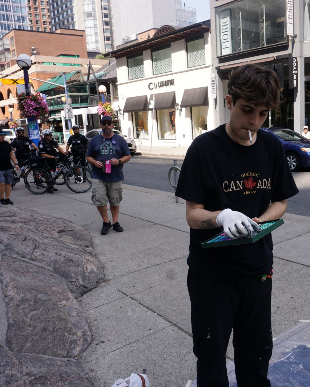 Louis painting on the street during the Yorkville Murals (YVM) Festival 2025: Smoking as police observe him