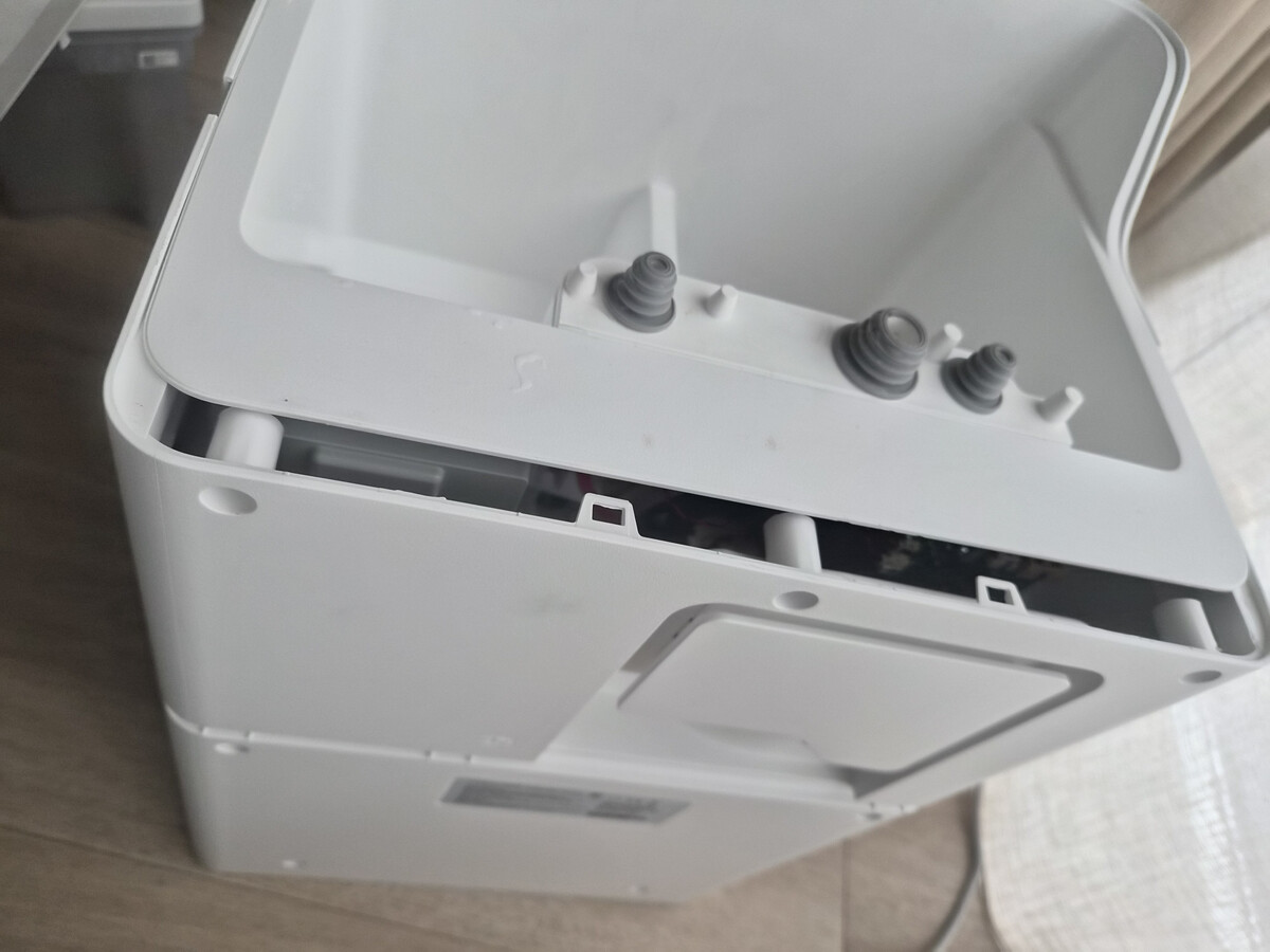 Upper edge of the Roborock dock's single-piece rear cover pulled away, exposing retaining windows.