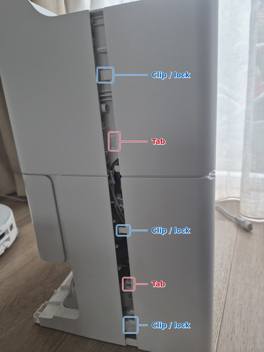 One side of the Roborock dock's wraparound rear cover partly released, with two tab groups marked in red and three clips or locks marked in blue.
