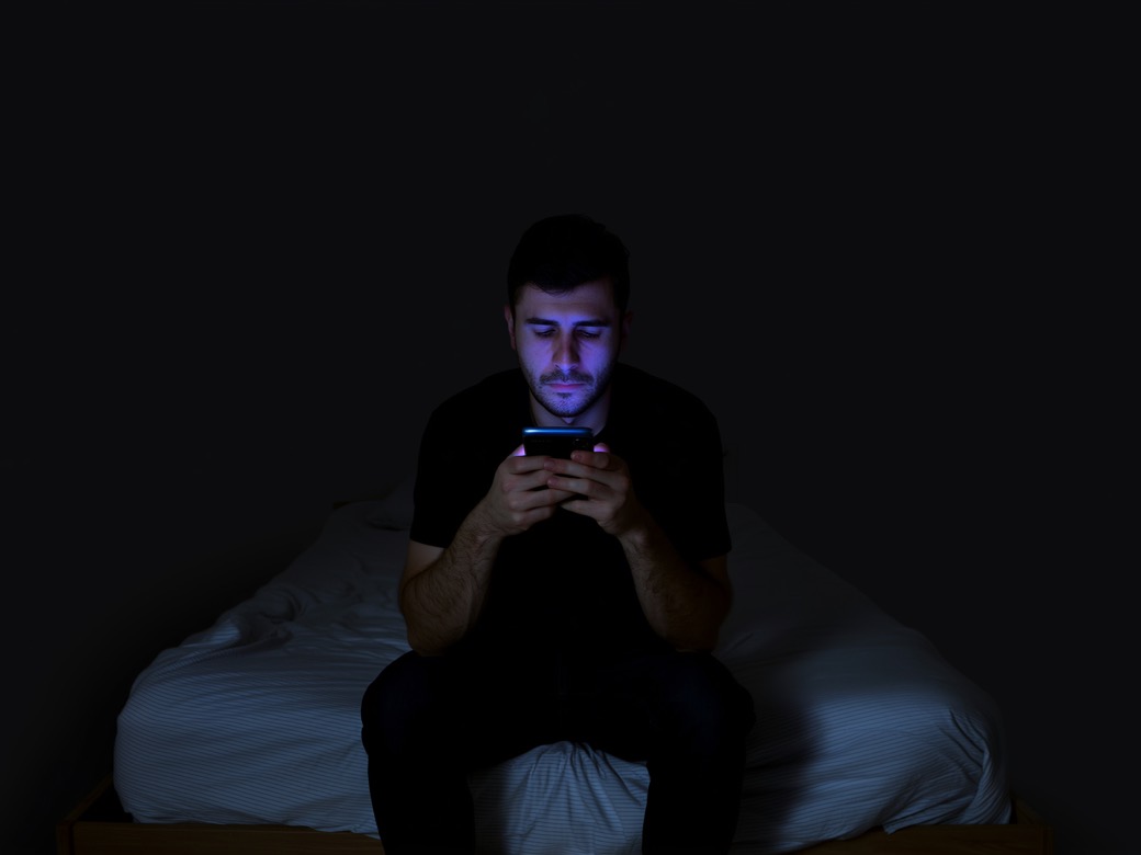 Homme seul dans le noir, le visage éclairé par son téléphone