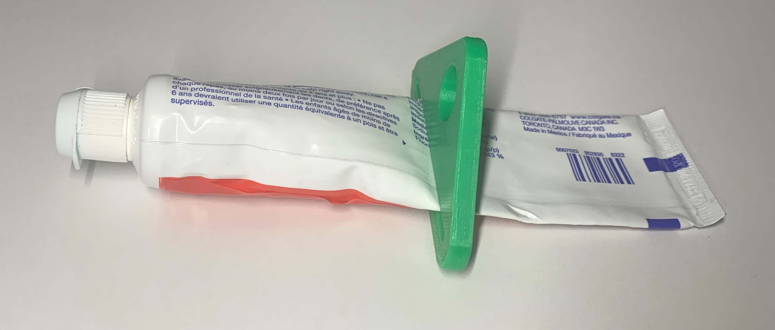 Picture of a green 3d printed toothpaste squeezer inserted midway along a tube of toothpaste.