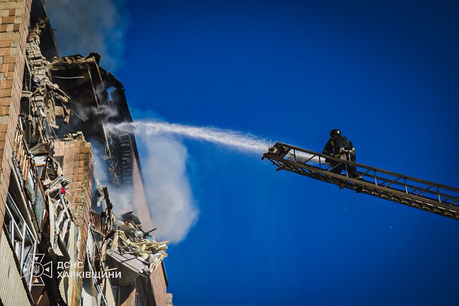 A firefighter on a turntable ladder plays a hose into a blasted upper floor of a Kharkiv apartment block on 12 October, the morning after an energy ceasefire was announced