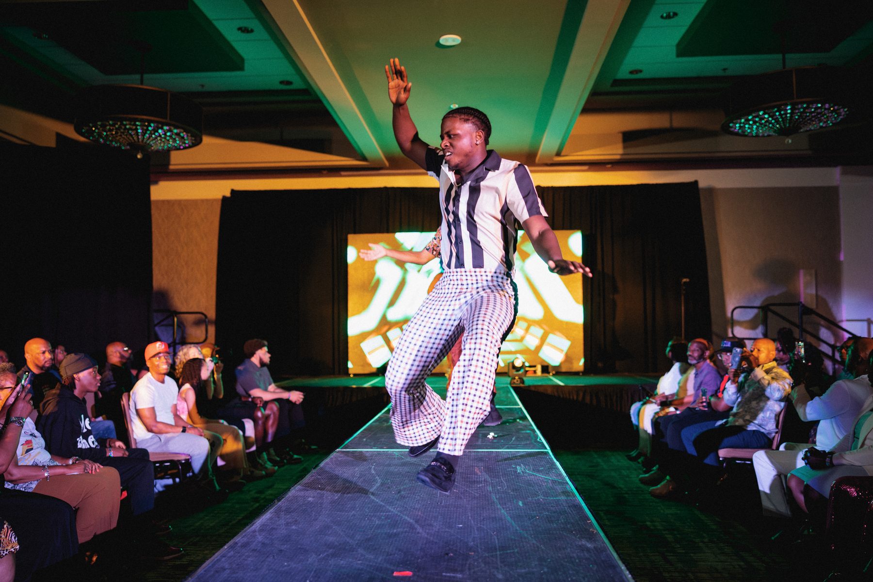 A young man dances down the runway in front of a full audience.