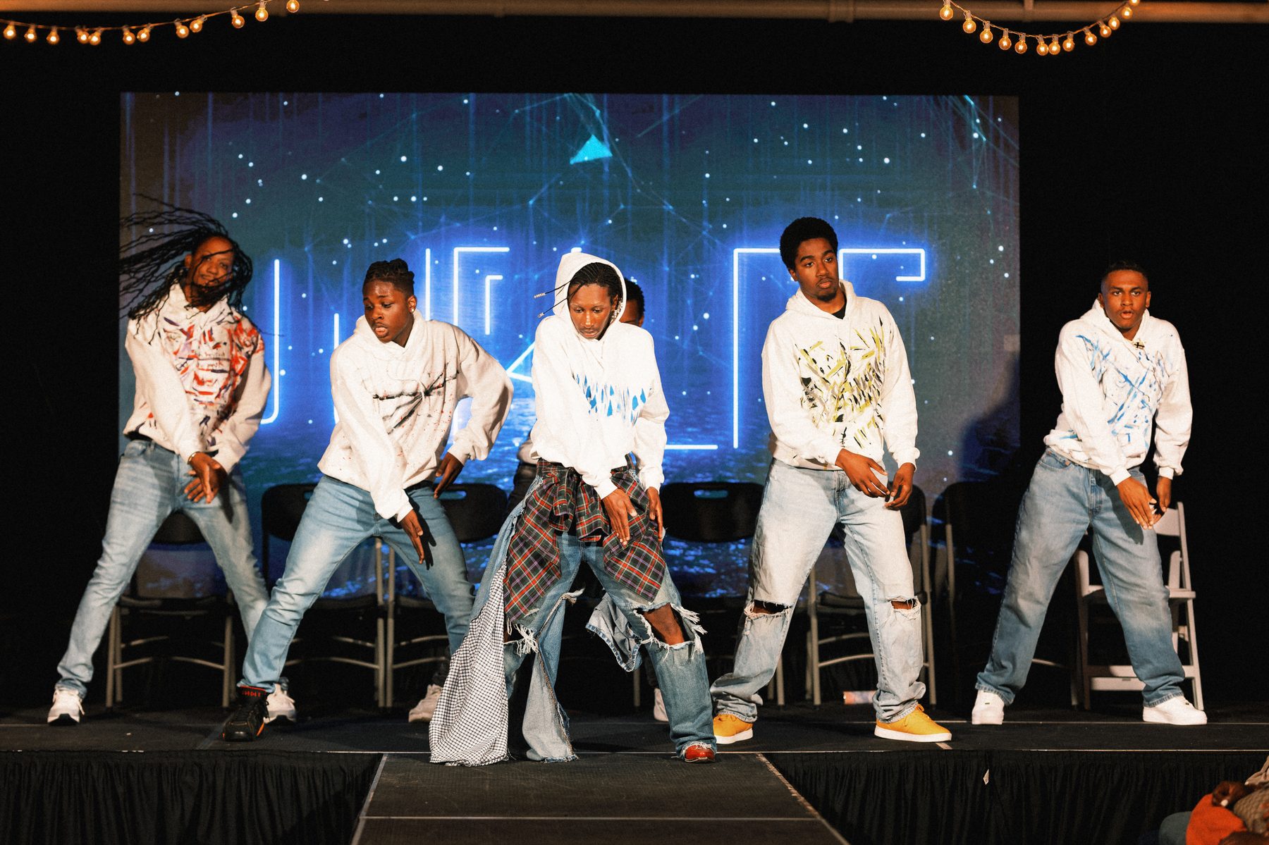 Five young men perform together on stage at TheGifted Arts in hand-painted hoodies.
