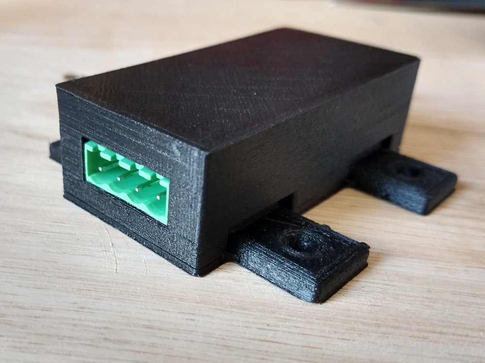 Photo of the assembled box. A black 3D printed box with the top and bottom put together (press-fit) is shown. In the clearing for the connector, you guessed it, there's the connector, flush with the edge of the enclosure.