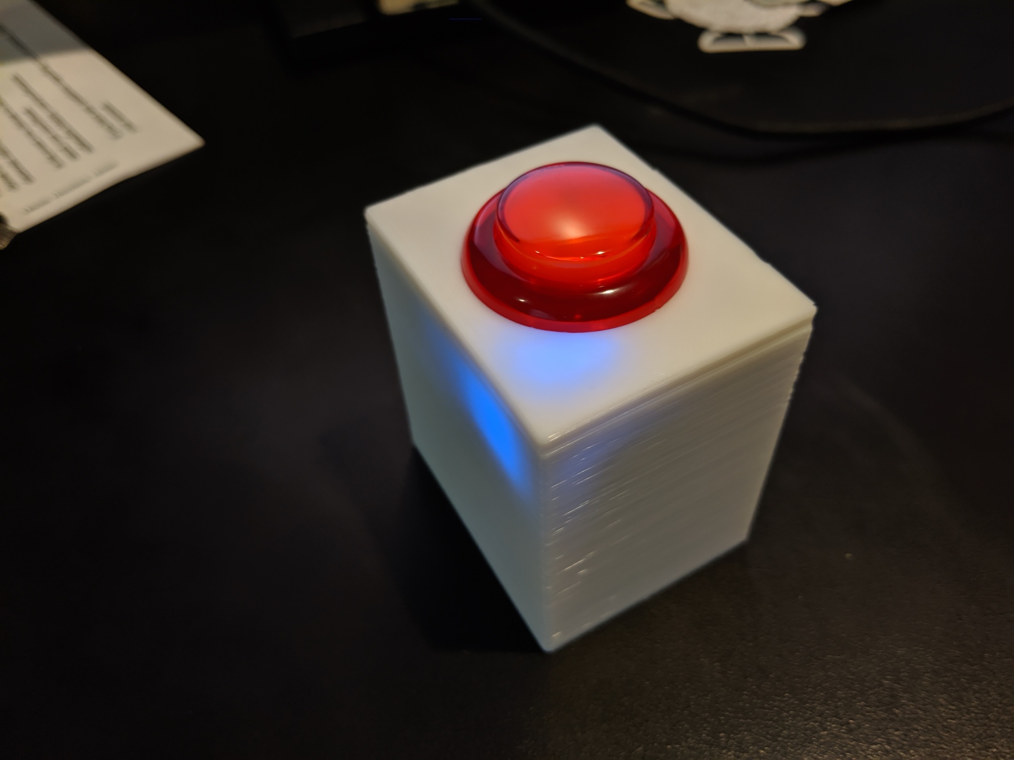 A 3D printed white box with a red arcade button on top resting on a black surface